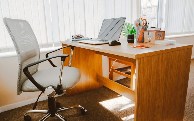A modern office workspace featuring a wooden desk, chair, laptop, and bright natural light.